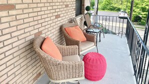A brick exterior wall with a balcony featuring wicker chairs, a small table, and a pink pouf. - Spacious comfort, 1st FL, parking, 2 TVs, laundry,Beautiful views of NYC skyline (Clifton)