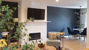 Una sala de estar moderna con un televisor de pantalla plana, un ventilador de techo y una zona de comedor con una mesa y sillas.