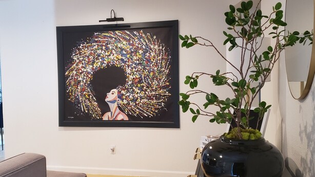 Una sala moderna con un cuadro abstracto de gran tamaño, un sofá gris, una consola negra con una planta y un espejo en la pared.