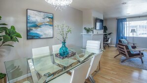 Un comedor moderno con una mesa de vidrio, sillas blancas, un jarrón azul con flores y una lámpara de araña contemporánea.