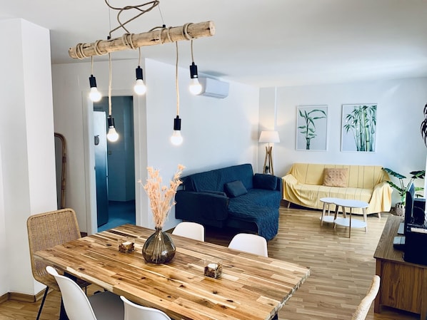 A modern living room with a wooden dining table, blue and yellow sofas, and a wooden floor.