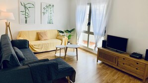 A living room with a sofa, a TV, a coffee table, and a plant. - Mediterranean apartment centrally located 500m beach (Sant Feliu de Guíxols)