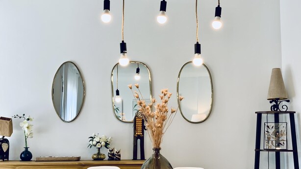 A dining area with a wooden table, three oval mirrors, and hanging lights. - Mediterranean apartment centrally located 500m beach (Sant Feliu de Guíxols)