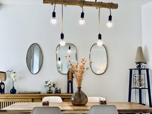A dining area with a wooden table, three oval mirrors, and hanging lights.
