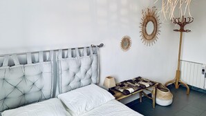 A bedroom with a tufted headboard, a bedside table with a lamp, a bench with a patterned cushion, and two wall decorations. - Mediterranean apartment centrally located 500m beach (Sant Feliu de Guíxols)
