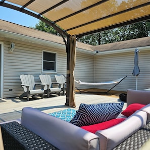 A covered outdoor seating area with a hammock, lounge chairs, and a sofa with patterned cushions.