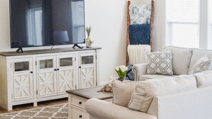 A modern living room with a flat-screen TV, white cabinetry, a beige sofa, a patterned rug, and a ceiling fan.