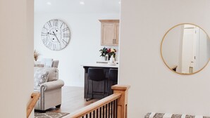 A modern interior with a staircase, a round mirror, and a dining area with a clock.