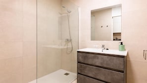 A modern bathroom with a glass-enclosed shower, a white sink with a mirror above, and a vanity with drawers.