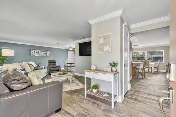 A living room with a grey sofa, a coffee table, and a dining area with a white table and chairs.