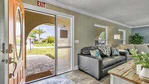 A living room with a sliding glass door leading to a patio, a grey leather sofa, and a wooden coffee table. - Beautiful Waterfront Pool Home | Close to Golf & Beaches | Dog Friendly | Free Wifi | Dock (Palm Coast)