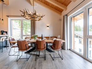 Uma sala de jantar com mesa de madeira, cadeiras de couro e lustre com chifres.