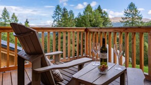 A wooden deck with two Adirondack chairs, a table with a bottle of wine, two wine glasses, and a bowl of fruit. - Luxurious chalet with sauna, near the ski slope (Turracher Höhe)