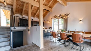 A modern kitchen with wooden beams, a dining area with a large table and chairs, and a staircase leading to an upper level. - Luxurious chalet with sauna, near the ski slope (Turracher Höhe)