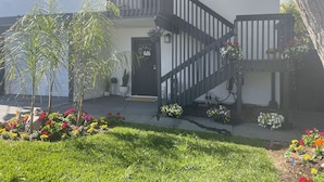A two-story house with a black staircase, a front door with a 'hello' sign, and a small garden with various flowers and plants. - Cheerful and Remodeled 3-bedroom beach cottage, STEPS to beach. Sleeps 9!  (Carlsbad)