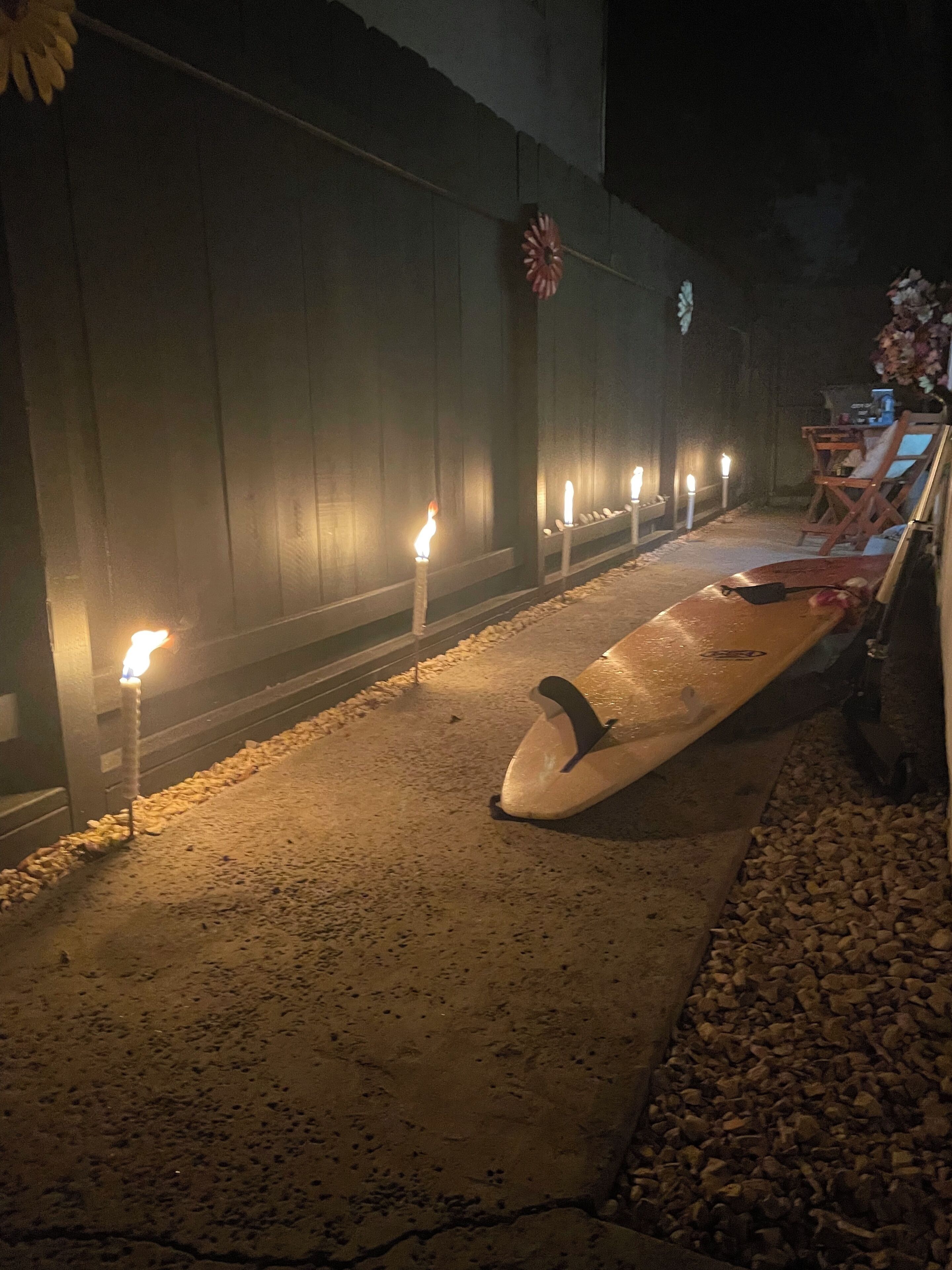 Een pad omzoomd met kaarsen dat leidt naar een strand met een surfplank en ligbedden.