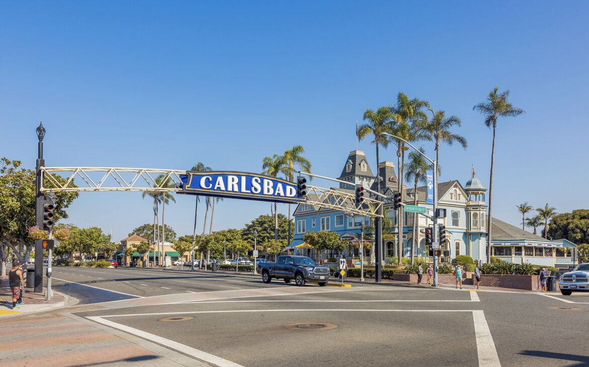 A street intersection with a blue sign reading "CARLSBAD" and a historic building with a blue facade.