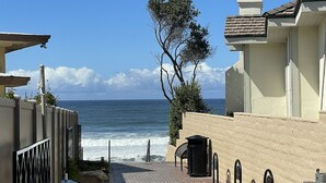 A coastal pathway leading to the sea with a view of the ocean, a tree, and a building with a chimney. - Cheerful and Remodeled 3-bedroom beach cottage, STEPS to beach. Sleeps 9!  (Carlsbad)