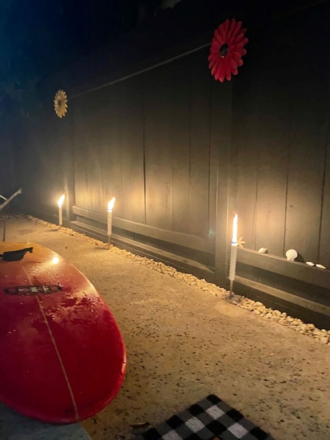 Un espacio al aire libre tenuemente iluminado, con un objeto rojo, posiblemente un vehículo, y un patrón a cuadros en el suelo.