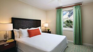 A neatly made bed with white linens and a red accent pillow, flanked by two bedside tables with lamps, in a room with green curtains and a patterned carpet. - **ATLANTIS BAHAMAS, PARADISE** - BEAUTIFUL 1 BEDROOM, SLEEPS 4+  (Paradise Island)