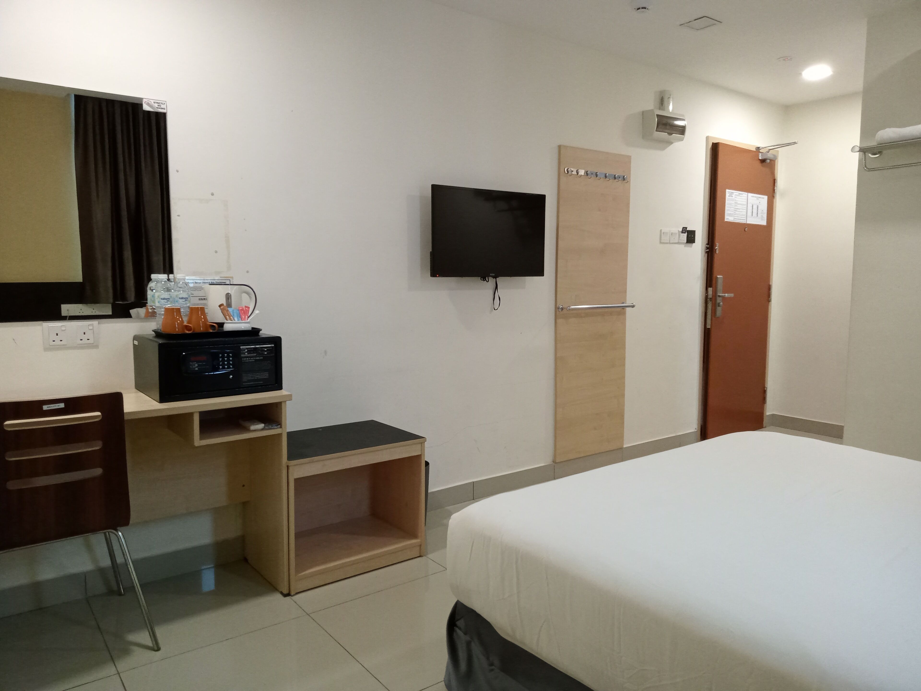 Habitación de hotel con cama, escritorio con computadora, televisión y puerta de madera.