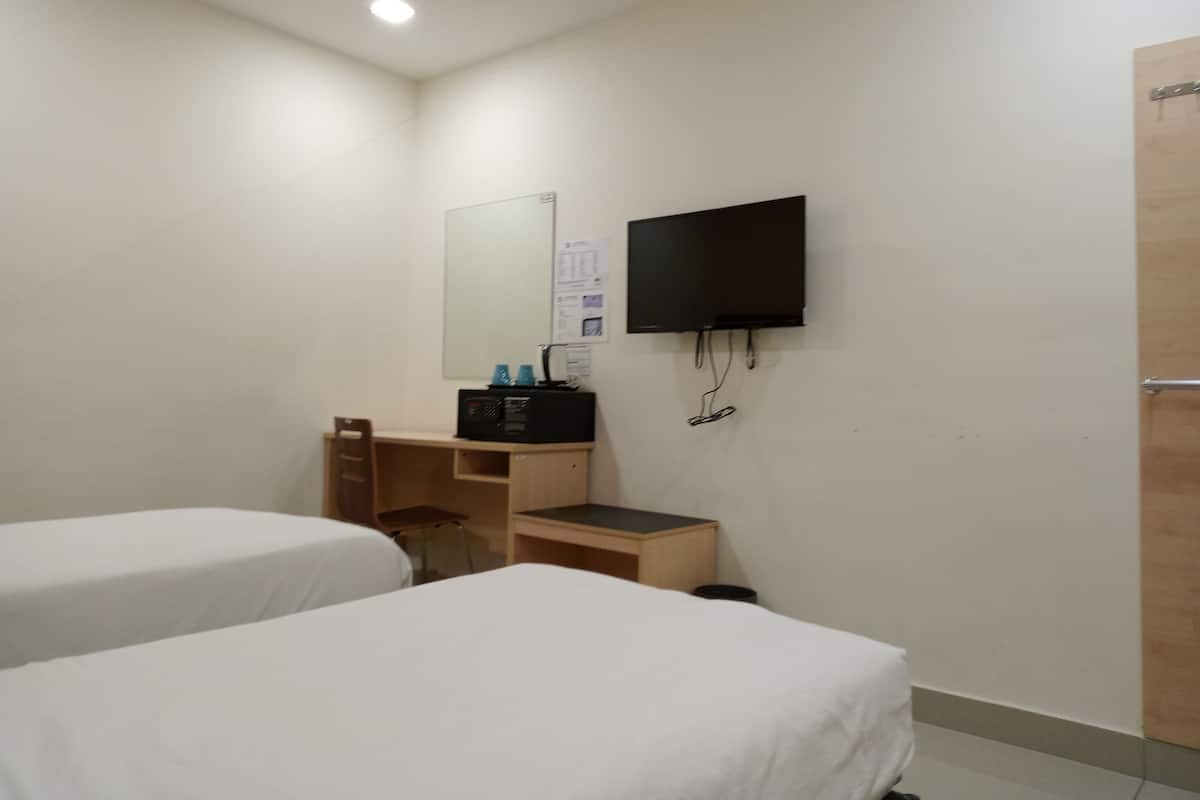 Hotellihuone, jossa on kaksi erillistä sänkyä, työpöytä tuolilla, seinälle asennettu taulutelevisio ja puinen ovi.