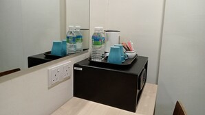 Habitación de hotel con minibar negro, un espejo y una mesa con botellas de agua, cafetera y taza.
