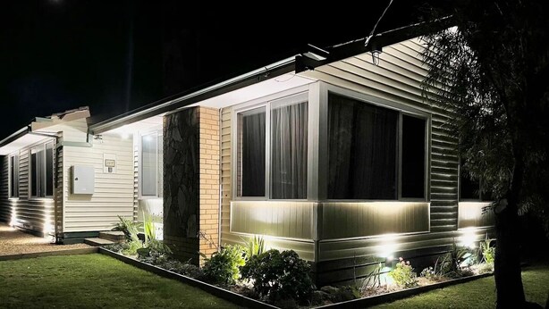 Una casa móvil moderna con un exterior bien iluminado, una pared de acento de ladrillo y un jardín delantero ajardinado.