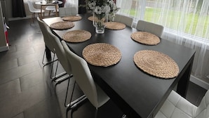 Un comedor con una mesa oscura, sillas blancas y individuales tejidas.
