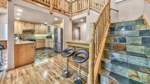 Una cocina amplia con armarios de madera, una isla central y una escalera con barandillas de madera.