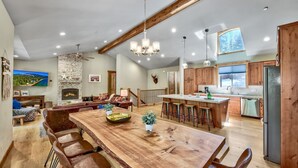 A spacious living area with a wooden dining table, comfortable seating, a fireplace, and a large window offering a view of the outdoors.