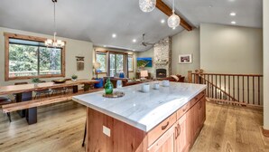 A spacious kitchen with a large island, wooden flooring, and a stone fireplace.