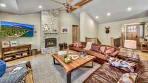 A spacious living room with a stone fireplace, leather sofas, a wooden coffee table, and a ceiling fan.