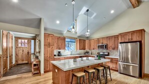A spacious kitchen with wooden cabinets, a large island with stools, stainless steel appliances, and pendant lighting.