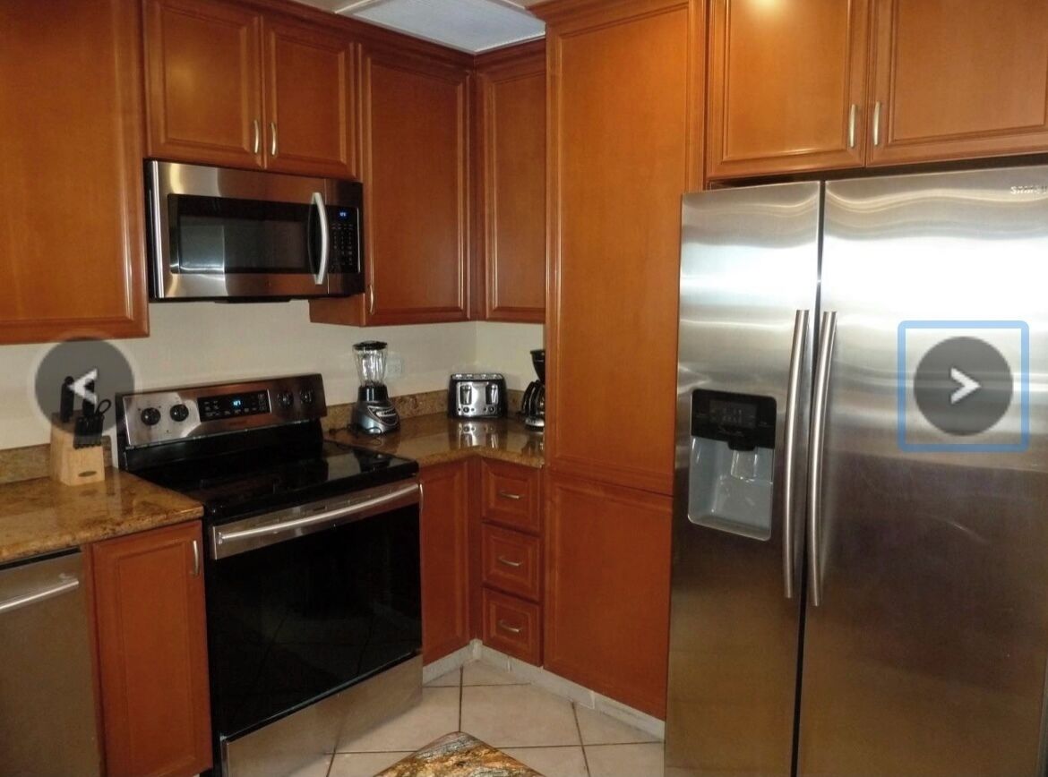 Una cocina con armarios de madera, electrodomésticos de acero inoxidable, incluyendo microondas, estufa y refrigerador, y encimera de granito.