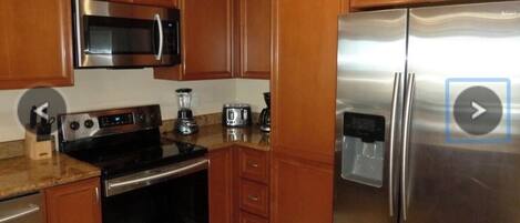 A kitchen with wooden cabinets, stainless steel appliances including a microwave, stove, and refrigerator, and a granite countertop.