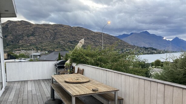 Eine Holzterrasse mit Tisch und Stühlen, mit Blick auf eine gebirgige Landschaft und ein Gewässer.
