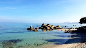 A coastal landscape with clear water, rocky formations, and a sandy beach.