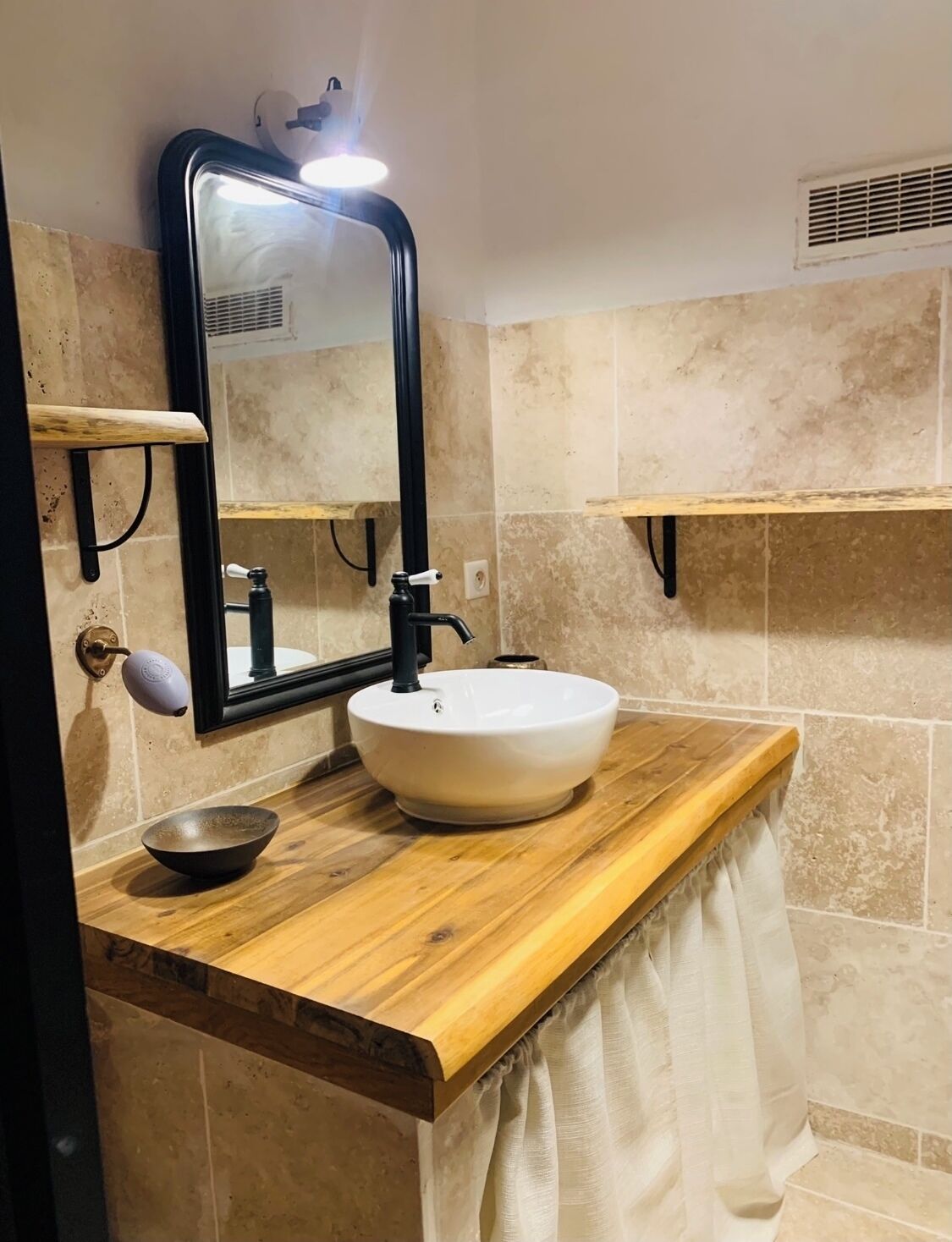 A bathroom with a wooden vanity, a white sink, a mirror, and beige tiled walls.