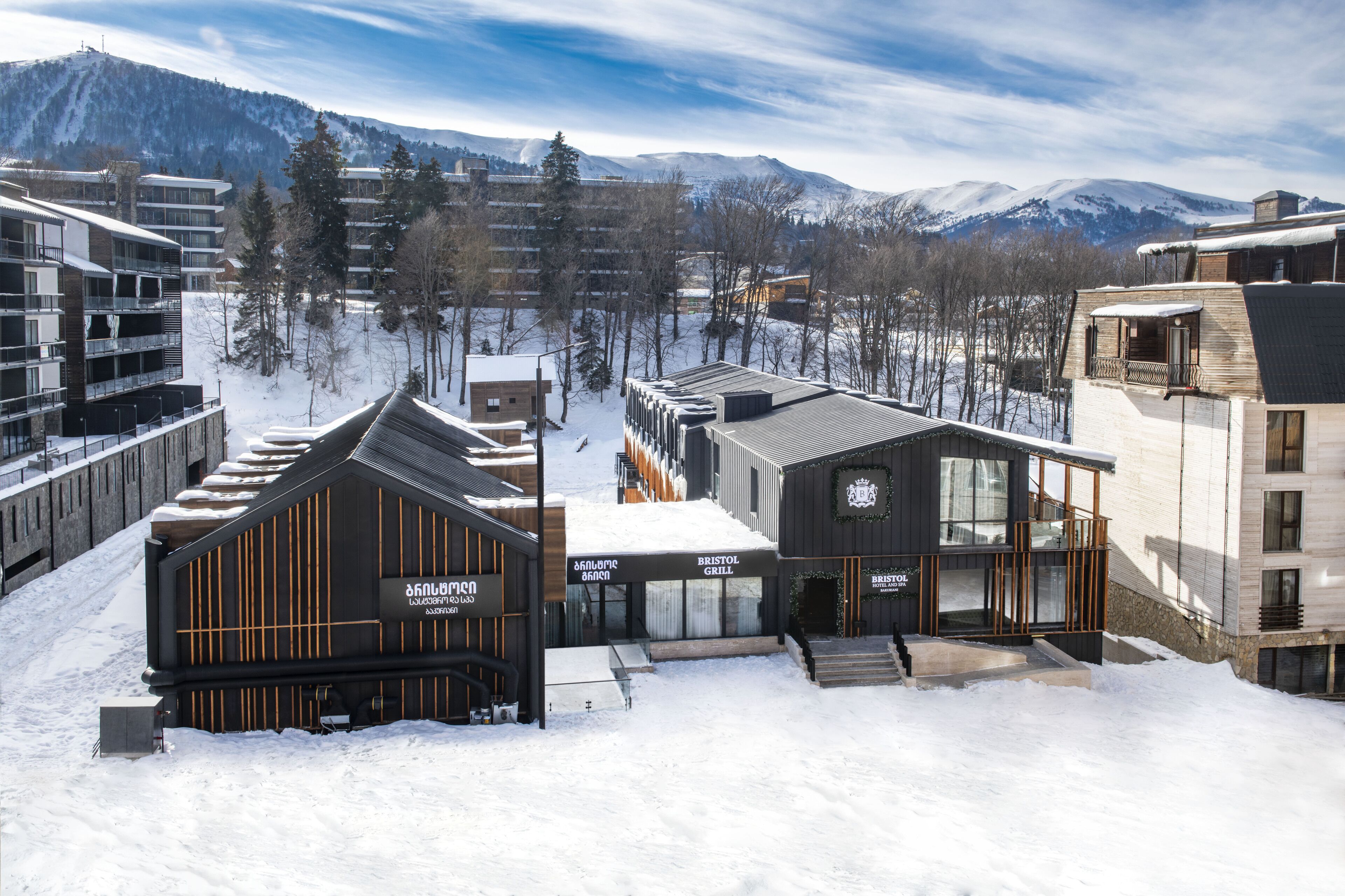 A modern building with a sign for 'Bristol Grill' and 'The Lodge' in a snowy setting with mountains in the background.
