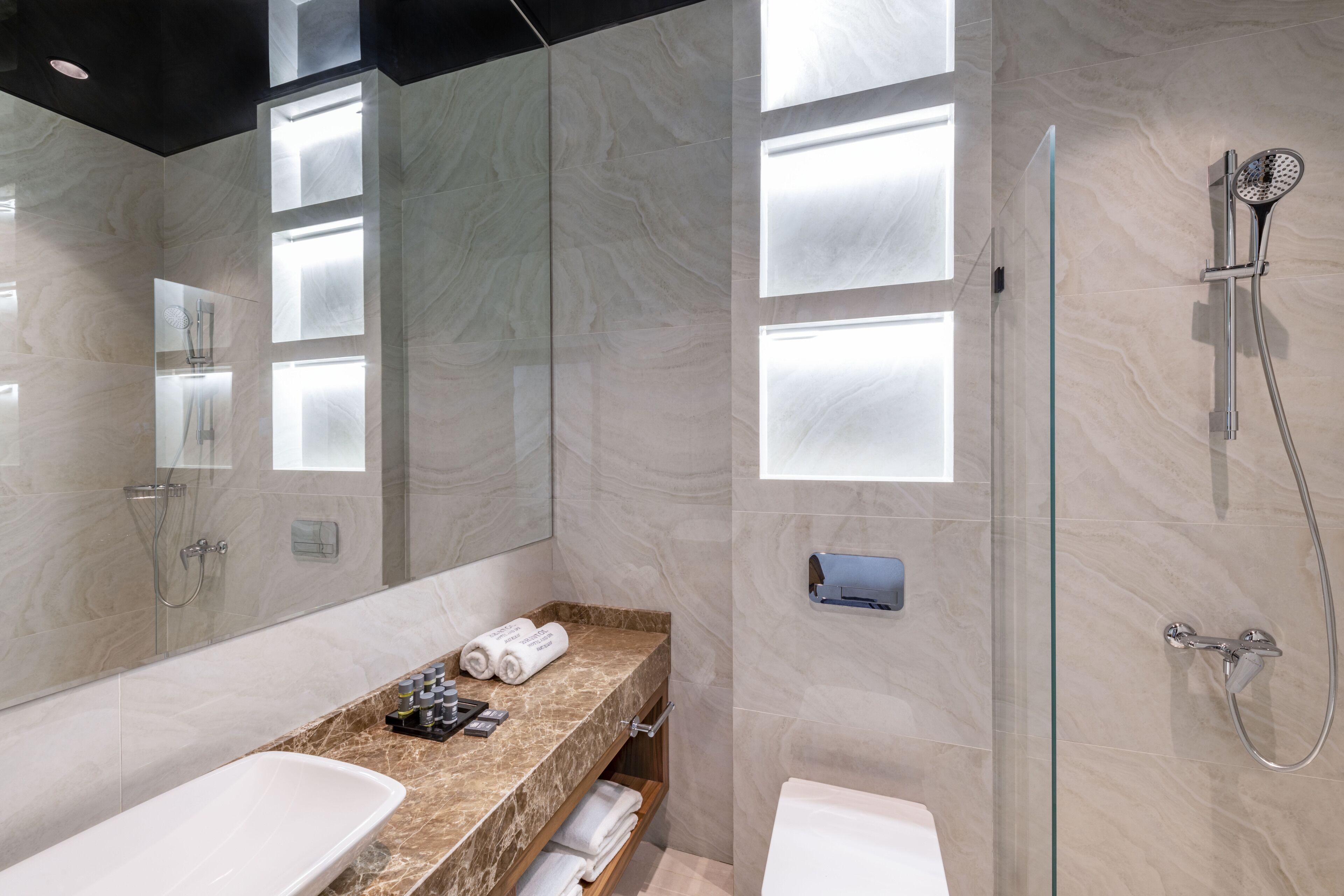 A modern bathroom with a marble vanity, a glass shower enclosure, and a large mirror.