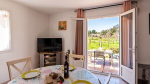 Un comedor con una mesa preparada para cuatro, un televisor y vistas a un jardín por una puerta abierta.