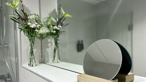 Ein Badezimmer mit weißem Waschtisch, einem Spiegel und einer Vase mit Blumen.