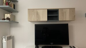 Ein modernes Wohnzimmer mit einem Flachbildfernseher, der an einem weißen Schrank befestigt ist, einem Holzschrank darüber und einem Heizkörper darunter.