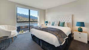 A bedroom with a large bed, a chair, a nightstand, and a view of mountains through a large window.