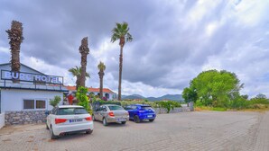 Et hotel med skilt, parkerede biler, palmer og et bjerglandskab i baggrunden.