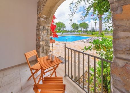 A balcony with a pool view, stone walls, and wooden furniture.