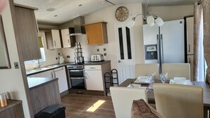 A compact kitchen with a stove, oven, and a microwave. There is a dining area with a table and chairs. - 2br-sleeps6-fireplace-parking-patio-seaside (Clacton-on-Sea)