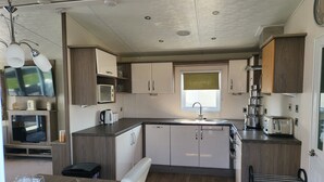 A compact kitchen with a sink, microwave, and toaster. There is a dining area with a table set for two. - 2br-sleeps6-fireplace-parking-patio-seaside (Clacton-on-Sea)
