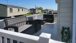A deck with outdoor furniture, a white railing, and a view of mobile homes in the background. - 2br-sleeps6-fireplace-parking-patio-seaside (Clacton-on-Sea)